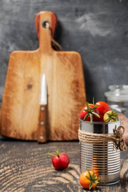 Teneke içinde kiraz domatesleri ve gri bir duvara karşı koyu ahşap bir masanın üzerinde bir kesme tahtası. Metin için boşluk.