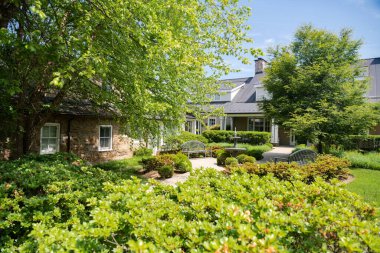 Yeşilliğe gömülü tek katlı bir ev. Büyük yeşil ağaçlar ve bir bahçe..