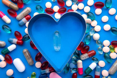 Mavi yüzeyde kalp şeklinde haplar ve kapsüller var. Sağlıklı kalp konsepti.