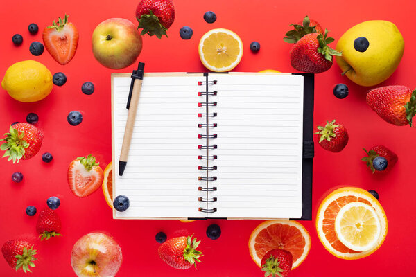 Summer fantasy. Fruits and berries on a red background. Notepad for text. Flying freshness. View from above. copyspace.