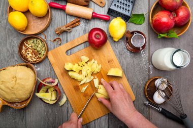 Kadının elleri ev yapımı elmalı turta yapmak için elma kesiyor. Tablonun ve malzemelerin üst görünümü.