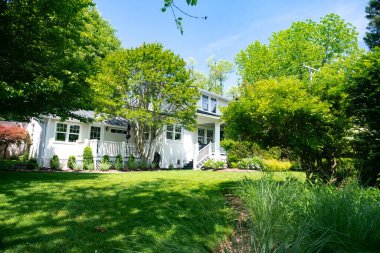 Beyaz tek katlı ev yeşilliğe gömülmüş, büyük yeşil çimenlikli..