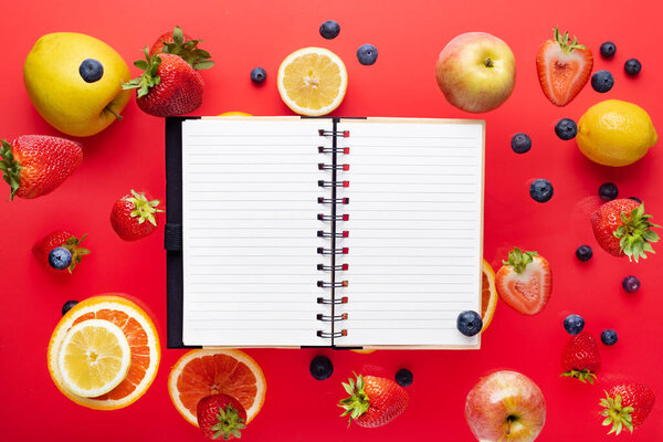Summer fantasy. Fruits and berries on a red background. Notepad for text. Flying freshness. View from above. copyspace.