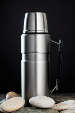 Çelik termos şişesi ahşap masada, siyah bir duvara karşı..