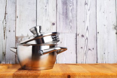 Ahşap bir masada cam kapaklı paslanmaz çelik tencere. Yan görünüm.