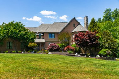 Kenar mahallelerde manzaralı ve ön bahçeli büyük lüks bir ev. Yaz günü, mavi gökyüzü.