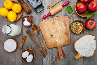 Mutfak masası elmalı turta yapma aşamasında. Un, merdane, süt, elma, yumurta ve mutfak gereçleri gri bir masada. Mesaj için yer var. Yukarıdan görüntüle.