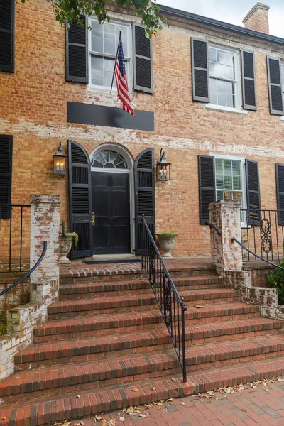 ポーチとアメリカの旗を持つ大きなレンガ造りの家への入り口のドア 黒のドア 窓とレンガの階段 — ストック写真