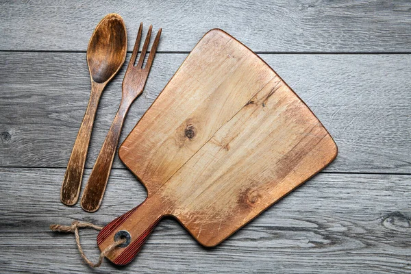 木制切菜板 灰色桌子上的木制勺子和叉子 从上面看复制空间 — 图库照片