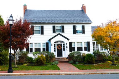 Yolun kenarındaki iki katlı tek aile evi. Sonbahar renklerinde çimenler ve ağaçlar