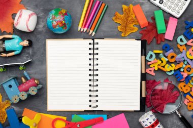 Kırtasiye, küre, ABC, oyuncaklar ve gri bir masanın üzerindeki açık not defteri. Yukarıdan bak. Özel metin için boşluk.