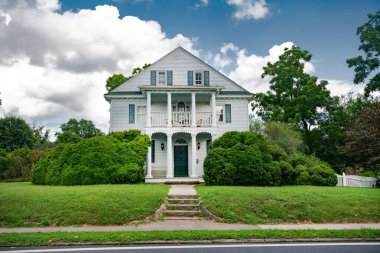 İki katlı, balkonlu ve kaplamalı geleneksel Amerikan tarzında verandalı bir ev. Ön bahçedeki çalılar ve budanmış çimenler.