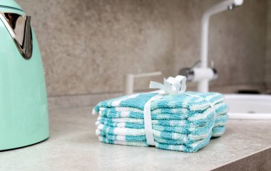 Lavabo ve çaydanlığın yanındaki mutfak masasında renkli havlu yığını. Metin için alanı kopyala.