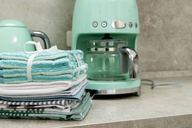 Modern bir mutfağın içinde mutfak havluları, kahve makinesi ve elektrikli su ısıtıcısı..