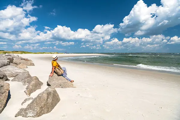 Μια Γυναίκα Καπέλο Κάθεται Μια Πέτρα Στην Ακτή Κοιτάζοντας Τον — Φωτογραφία Αρχείου