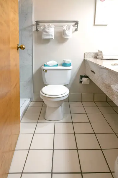 bathroom and toilet are tiled with white tiles and have a large mirror in front of the sink.