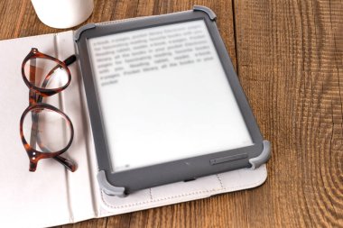 E-kitap okuyucu ve gözlükler ahşap bir masada..