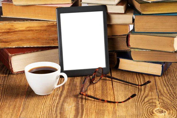 E-reader and stacks of vintage books on the desk. Glasses and a cup of coffee.Electronic technology concept. Space for text.