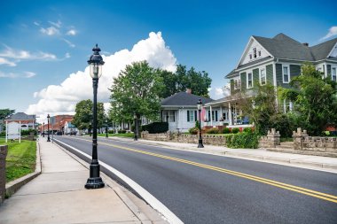Küçük bir Amerikan şehrinde sarı şeritli asfalt yol. Mavi bulutlu gökyüzü.