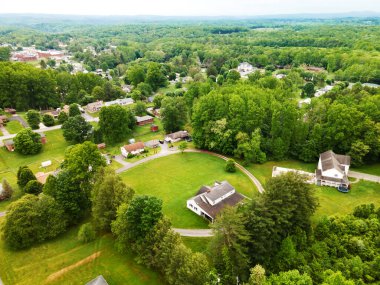 Kırsal yaz manzarası. Yeşilliklerle çevrili evlerin çatıları ve yolları. Bir İHA görüntüsü.