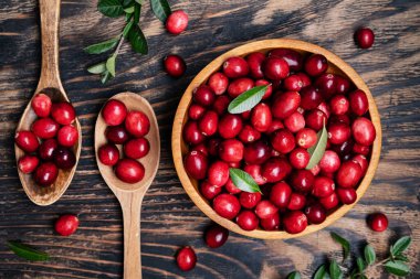 Koyu ahşap masada kaşıkla ahşap bir kasede taze kızılcıklar. Yukarıdan görüntüle. Metin için boşluk.