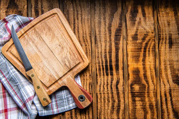 Wood cutting board with linen napkin and knife on wooden table with copy space, top view