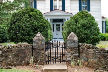 Taş çitli ve demir kapılı bir evin ön kapısı. Girişte çalılar olan taş basamaklar..