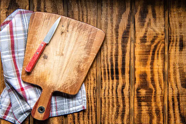 Wood cutting board with linen napkin and knife on wooden table with copy space, top view