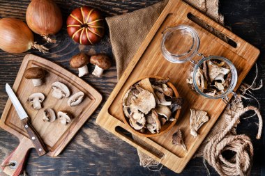 Tahta bir kasede ve kesme tahtasında çeşitli kurutulmuş mantarlar. Yukarıdan görüntüle.