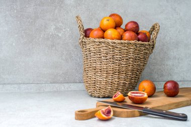 Kan portakalları sepette ve portakal dilimlerinde. Gri masa üzerinde bıçak. Mesaj için yer var..