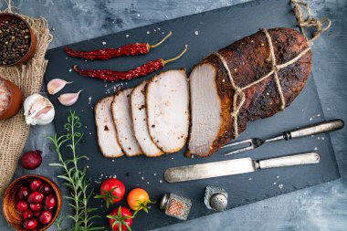 Dilimlenmiş dumanlı ve kaynamış domuz eti ve siyah bir taş tahtada biberiye. Biber ve kiraz domatesli. Yukarıdan görüntüle.