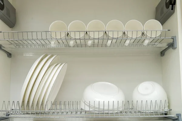 Metal rack for drying dishes with large beautiful white clean plates and glasses. Traditional comfortable kitchen.