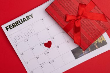 14 Şubat takvim şablonu kalp şeklinde ve kırmızı arka planda hediye. Düz yatış modeli, üst manzara. Sevgililer Günü konsepti