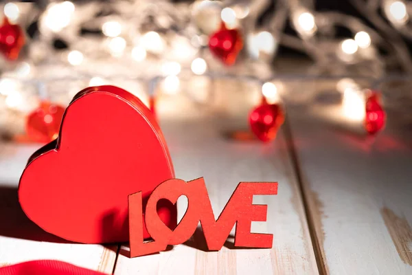 Word LOVE and red heart on wooden table against defocused bokeh light background. Love, valentine\'s day concept.