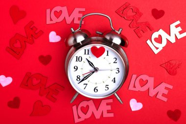 Sevgililer Günü. Kırmızı arka planda çalar saat, kalpler ve aşk kelimesi. Metin için boşluk.