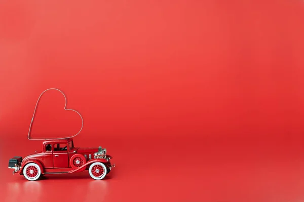 Red retro car delivering  red heart on  red background. The concept of the holiday Valentine\'s Day and Women\'s Day. Space for text.