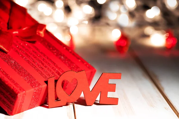 Word LOVE and red gift box on wooden table against defocused bokeh light background. Love, valentine\'s day concept.