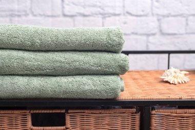 Hasır komodinin üzerindeki havlular beyaz tuğla duvara karşı. Metin için boşluk.