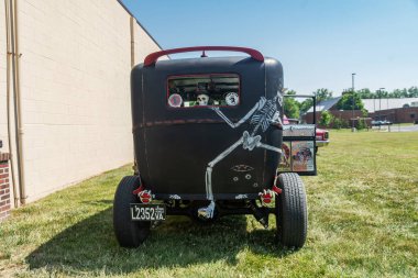 Kapısı açık siyah bir retro araba, kırmızı tekerlekler ve kafatası ve farları olan iskeletler. Arka plan.