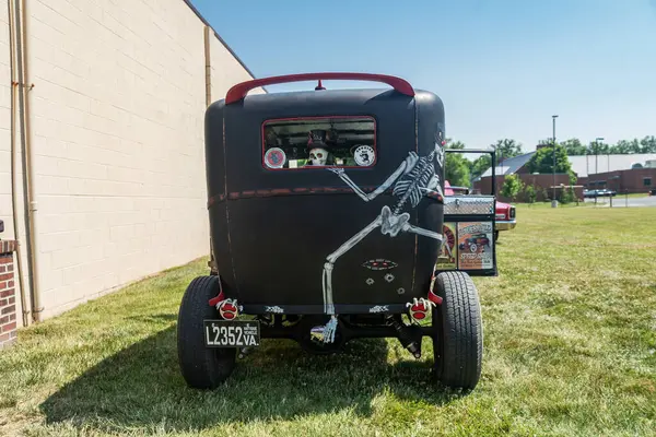 Kapısı açık siyah bir retro araba, kırmızı tekerlekler ve kafatası ve farları olan iskeletler. Arka plan.