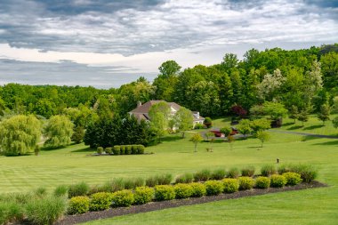 Mavi gökyüzünün altındaki lüks kır evi. Geniş çimleri biçilmiş bir manzara.