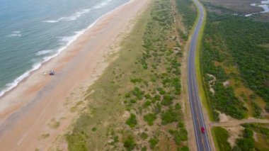 Kuzey Carolina 'da okyanus kıyısı boyunca uzanan bir yol. Sarı kum, okyanus, yeşil çimenler, otoyoldaki arabalar. Drone fotoğrafçılığı