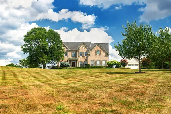 Brick country house with a large lawn against a background of blue clouds.