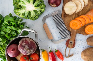 Sebzeler için dalgalı bıçak. Kesme tahtasındaki havuç dilimleri ve patatesler. Tencere, soğan, brokoli, domates ve maydanoz..