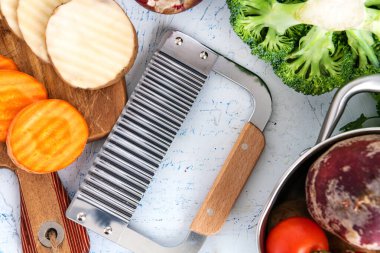 Sebzeler için dalgalı bıçak. Kesme tahtasındaki havuç dilimleri ve patatesler. Tencere, soğan, brokoli, domates ve maydanoz..