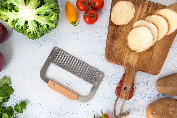 wavy knife for curly slicing vegetables. Potato slices on a cutting board. Onions, broccoli and parsley top view.