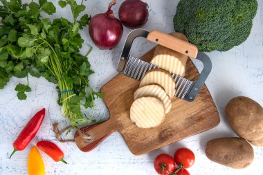 Kıvırcık sebzeler için dalgalı bıçak. Kesme tahtasındaki patates dilimleri. Soğan, brokoli ve maydanoz..