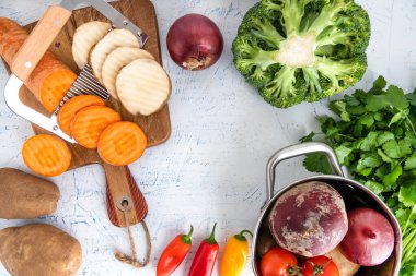 Sebzeler için dalgalı bıçak. Kesme tahtasındaki havuç dilimleri ve patatesler. Tencere, soğan, brokoli, domates ve maydanoz..