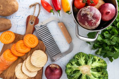 Sebzeler için dalgalı bıçak. Kesme tahtasındaki havuç dilimleri ve patatesler. Tencere, soğan, brokoli, domates ve maydanoz..