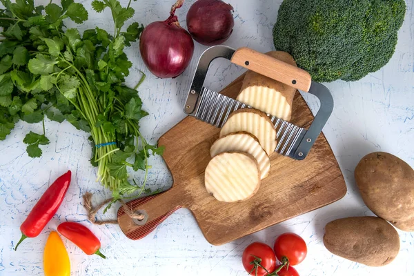 Kıvırcık sebzeler için dalgalı bıçak. Kesme tahtasındaki patates dilimleri. Soğan, brokoli ve maydanoz..